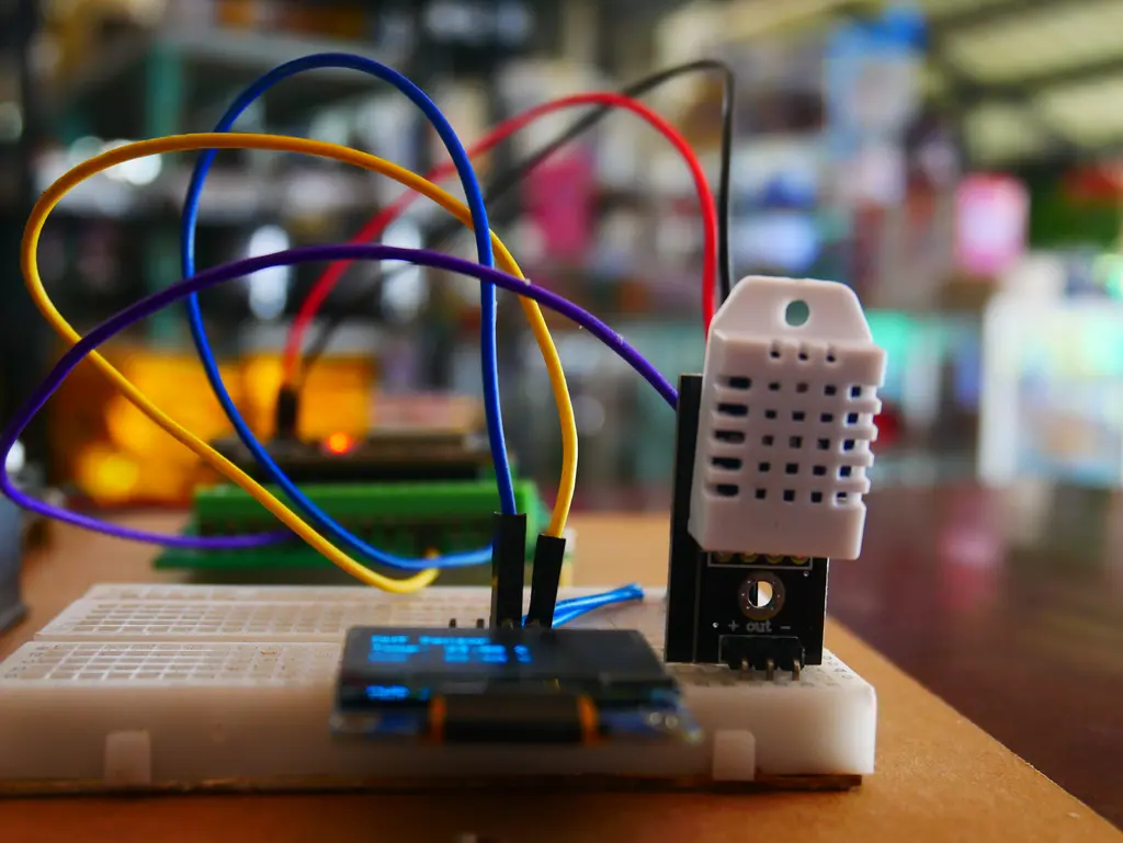 เซนเซอร์ DHT22 เชื่อมต่อกับ ESP32 และจอ OLED 128x64 มุมมองด้านข้าง เห็นการต่อสาย Jumper บน breadboard